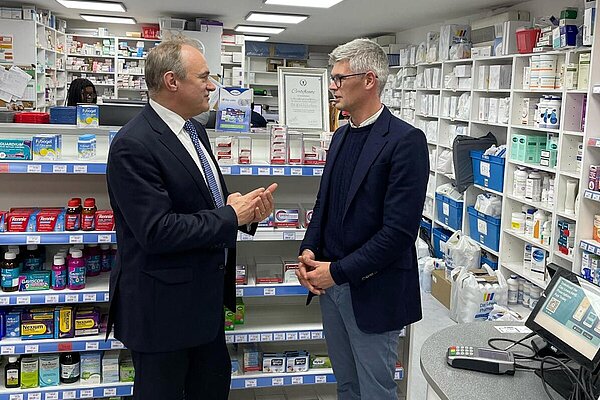 Al standing with the leader of the Lib Dems inside a pharmacy